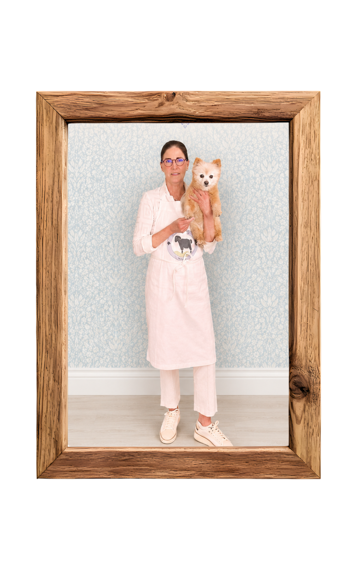 A square wooden picture frame with a natural brown wood grain border, containing a photo of a woman in a white nurse-style uniform holding a small fluffy light brown dog against a pale blue patterned wall.