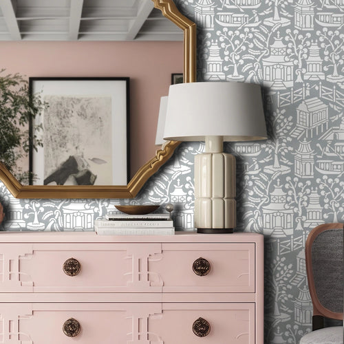 Asian garden wall stencil applied in a styled interior corner featuring a pink dresser, a white table lamp with a ribbed cream base, a gold-framed mirror, and natural light highlighting the gray and white painted stencil on the wall.