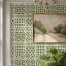 Bamboo wall stencil in a dining room, styled with a framed landscape painting and a green plant, and natural light highlighting the green and white painted stencil on the wall.