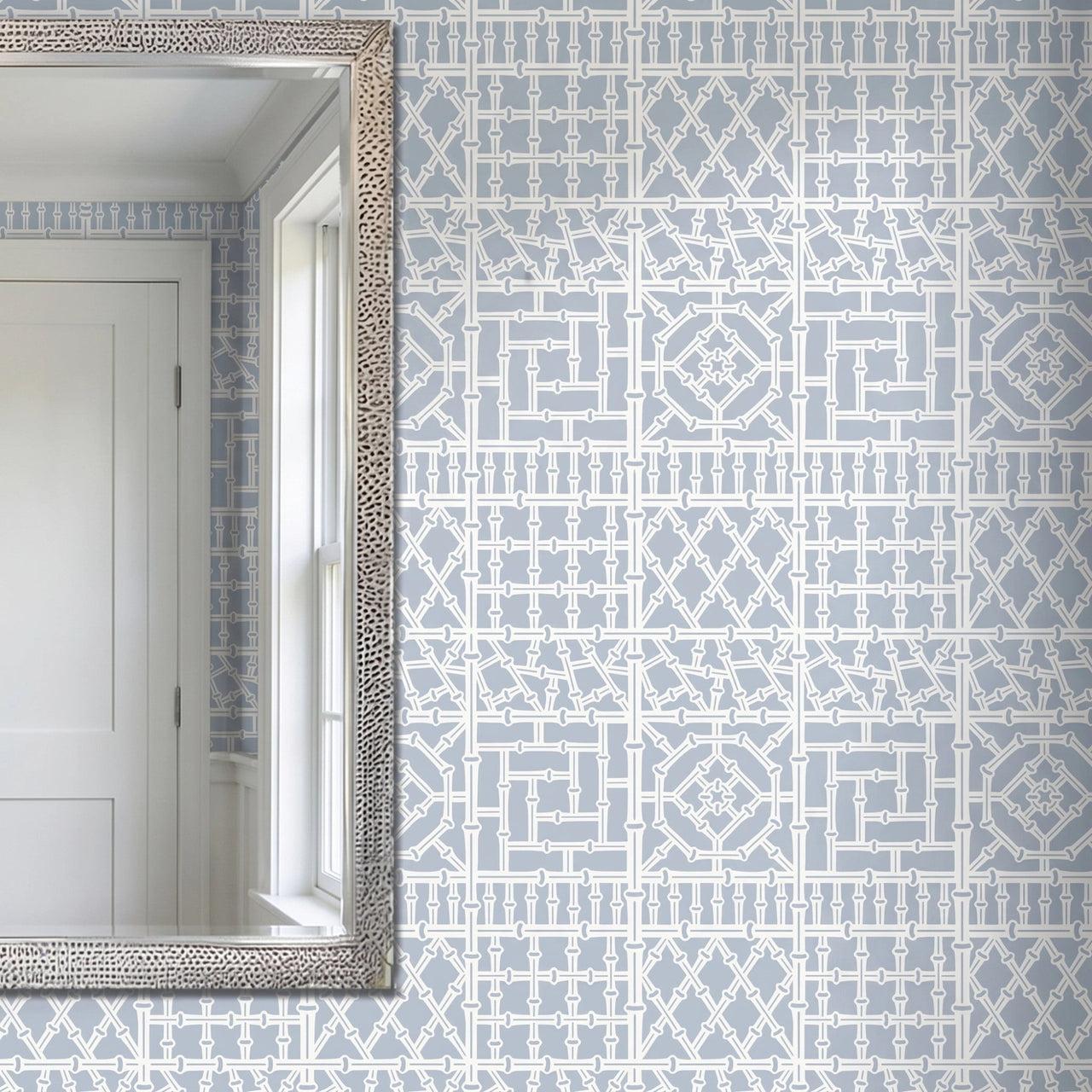 Bamboo wall stencil applied on a wall next to a silver-framed mirror reflecting a white door and window, and natural light highlighting the blue and white painted stencil.
