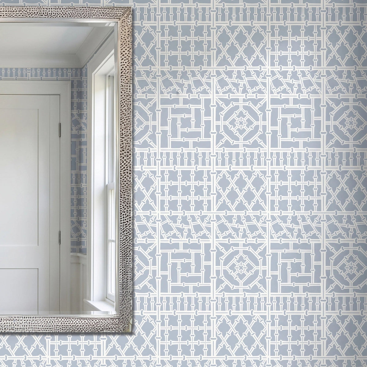 Bamboo wall stencil applied on a wall next to a silver-framed mirror reflecting a white door and window, and natural light highlighting the blue and white painted stencil.