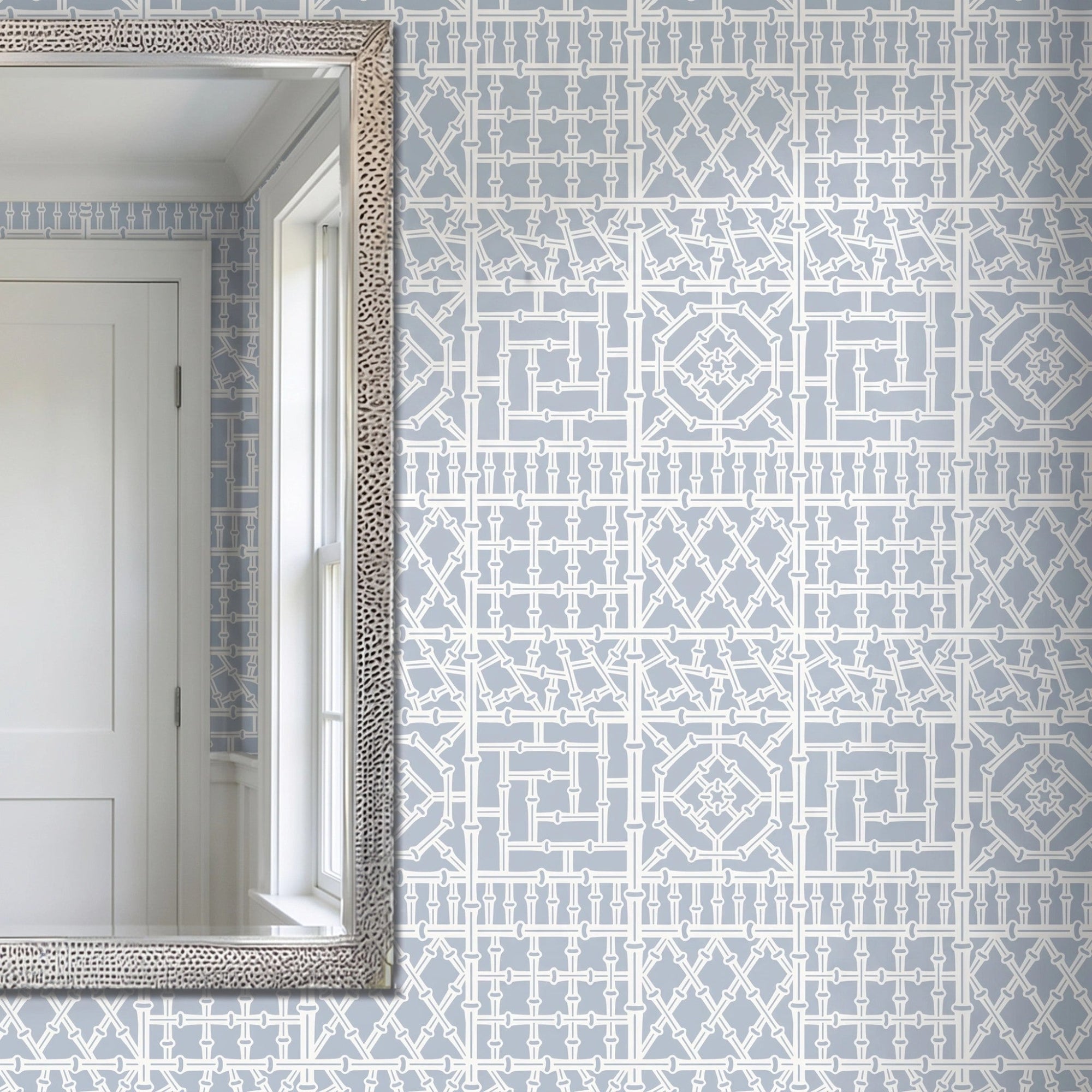 Bamboo wall stencil applied on a wall next to a silver-framed mirror reflecting a white door and window, and natural light highlighting the blue and white painted stencil.