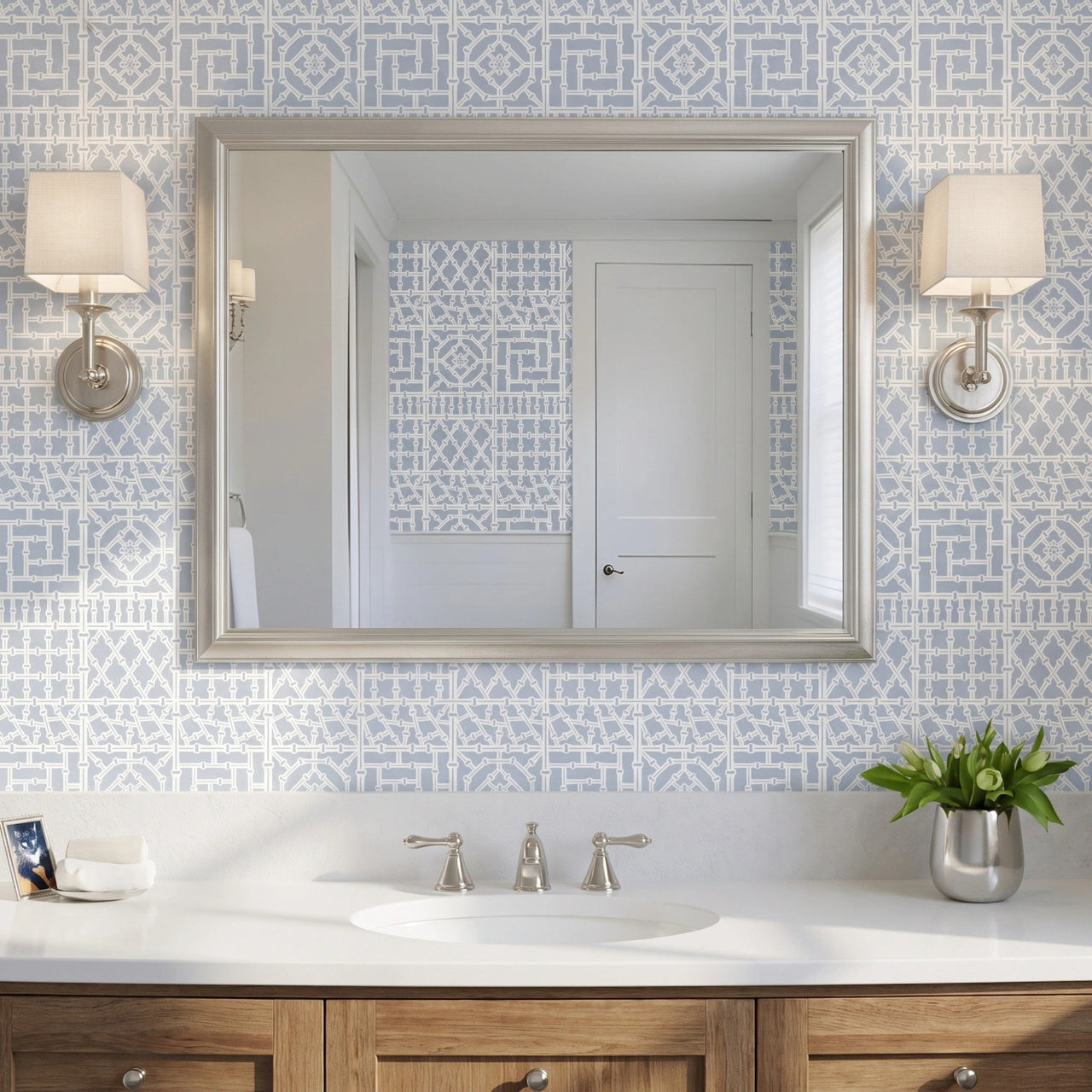 Bamboo wall stencil applied on a wall behind a silver-framed mirror reflecting a white door and window, sconces on each side of the mirror and natural light highlighting the blue and white painted stencil.