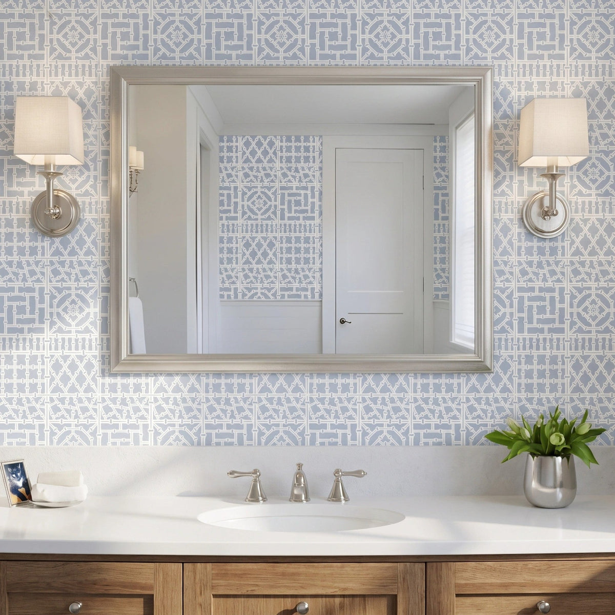 Bamboo wall stencil applied on a wall behind a silver-framed mirror reflecting a white door and window, sconces on each side of the mirror and natural light highlighting the blue and white painted stencil.