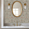 Birds and berries wall stencil applied in a powder room with an oval mirror with a gold frame featuring a repeating pattern of birds, flowers, and leaves in muted green and pink tones painted stencil on the wall.