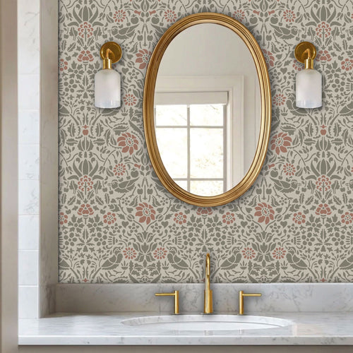 Birds and berries wall stencil applied in a powder room with an oval mirror with a gold frame featuring a repeating pattern of birds, flowers, and leaves in muted green and pink tones painted stencil on the wall.