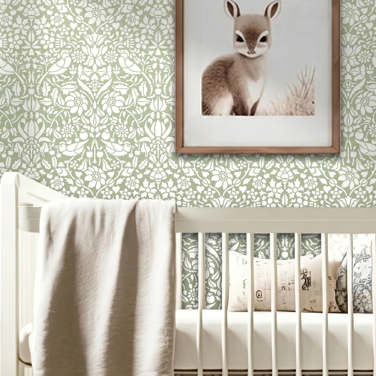 Birds and berries wall stencil in a nursery with a white wooden crib with a draped beige blanket, a framed print of a fawn hangs on the wall above the crib, and natural light highlighting the soft green and white painted wall stencil on the wall.