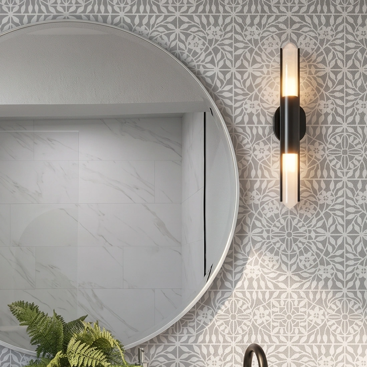 A modern wall-mounted sconce with a black metal frame and two vertical frosted glass lights emitting warm light, mounted on the wall painted with botanical tile wall stencil in grey next to a large round mirror.