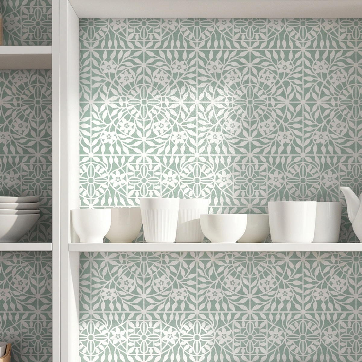 White ceramic bowls and cups displayed on open white shelves against a wall covered in botanical tile wall stencil in  green and white geometric floral tile pattern.