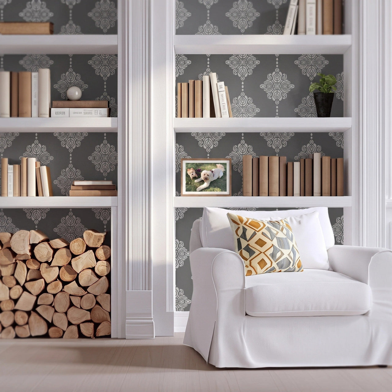 Damask block print wall stencil applied behind a white built-in bookshelves, books, firewood stack, and a white armchair with natural light highlighting the dark gray and light gray paint stencil painted on the wall behind the built-in shelves.