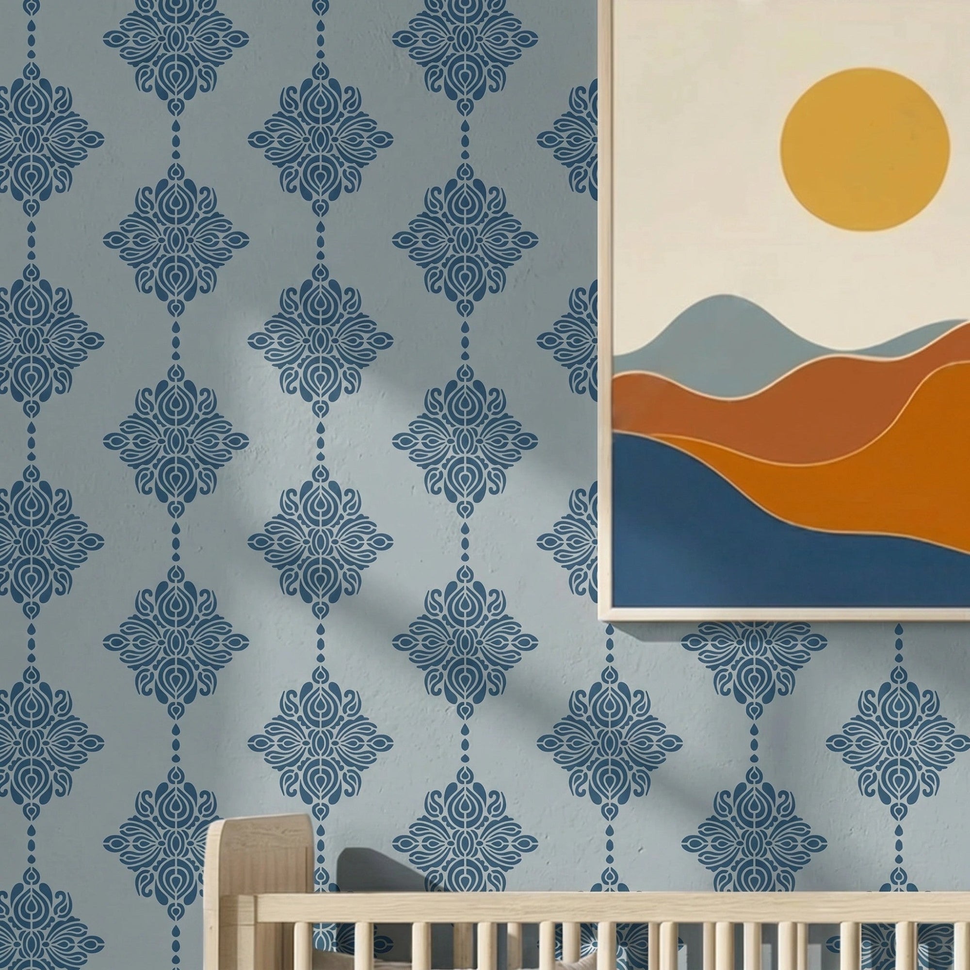 Damask block print stencil applied in a nursery, styled with a minimalist framed art print of rolling hills and a sun, and the top of a light wood crib, with natural light highlighting the dark blue on light blue stencil painted on the wall.