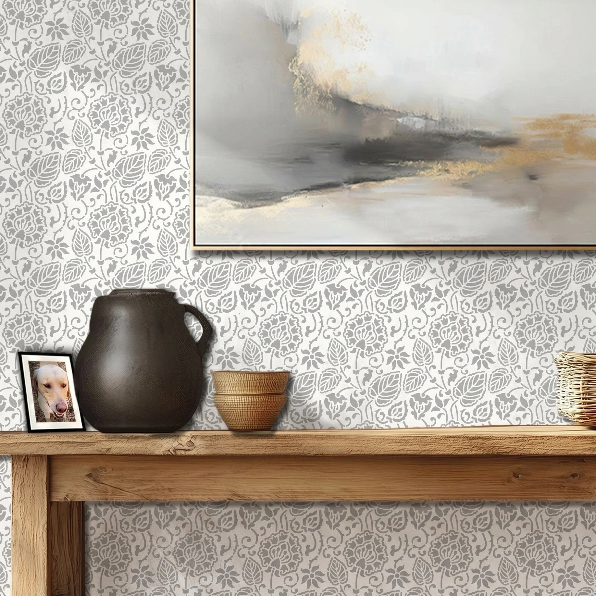 Dandelion wall stencil featured in a hallway with a wooden console table, a dark ceramic pitcher, a small woven bowl, and a framed abstract painting on the wall, with natural light highlighting the gray and white stencil painted on the wall.