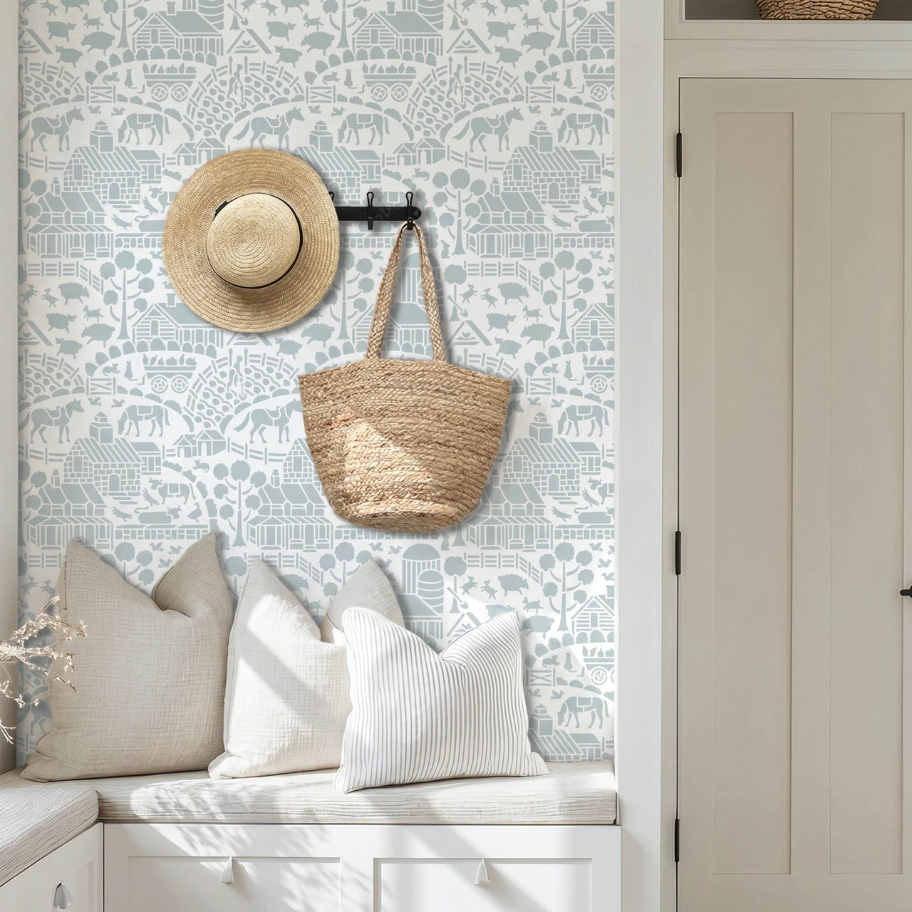 Day at the farm farmhouse wall stencil applied in a mudroom with pillows, a hat and basket hanging on the wall, and natural light highlighting the light blue and white painted stencil on the wall.