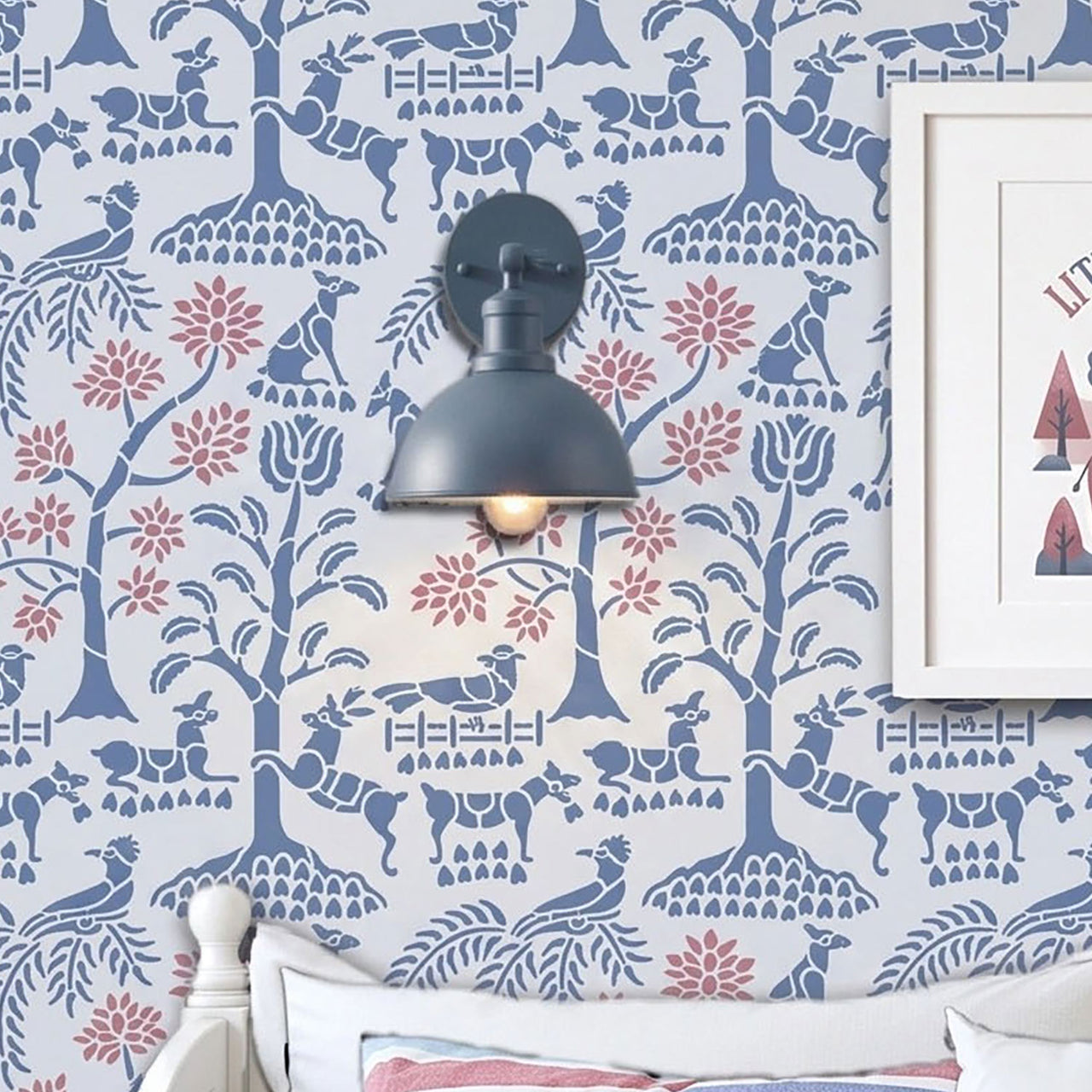 Enchanted forest wall stencil applied in a child's bedroom with a dark blue wall sconce mounted on it, plus part of a white bed and framed artwork visible, and the wall scone in on and highlighting the blue and pink painted wall stencil on the wall.