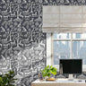 Enchanted forest wall stencil  featured in an office with a window and a beige roman shade, a desk with a computer monitor, small plants, and natural light highlighting the charcoal and light grey painted stencil on the wall.