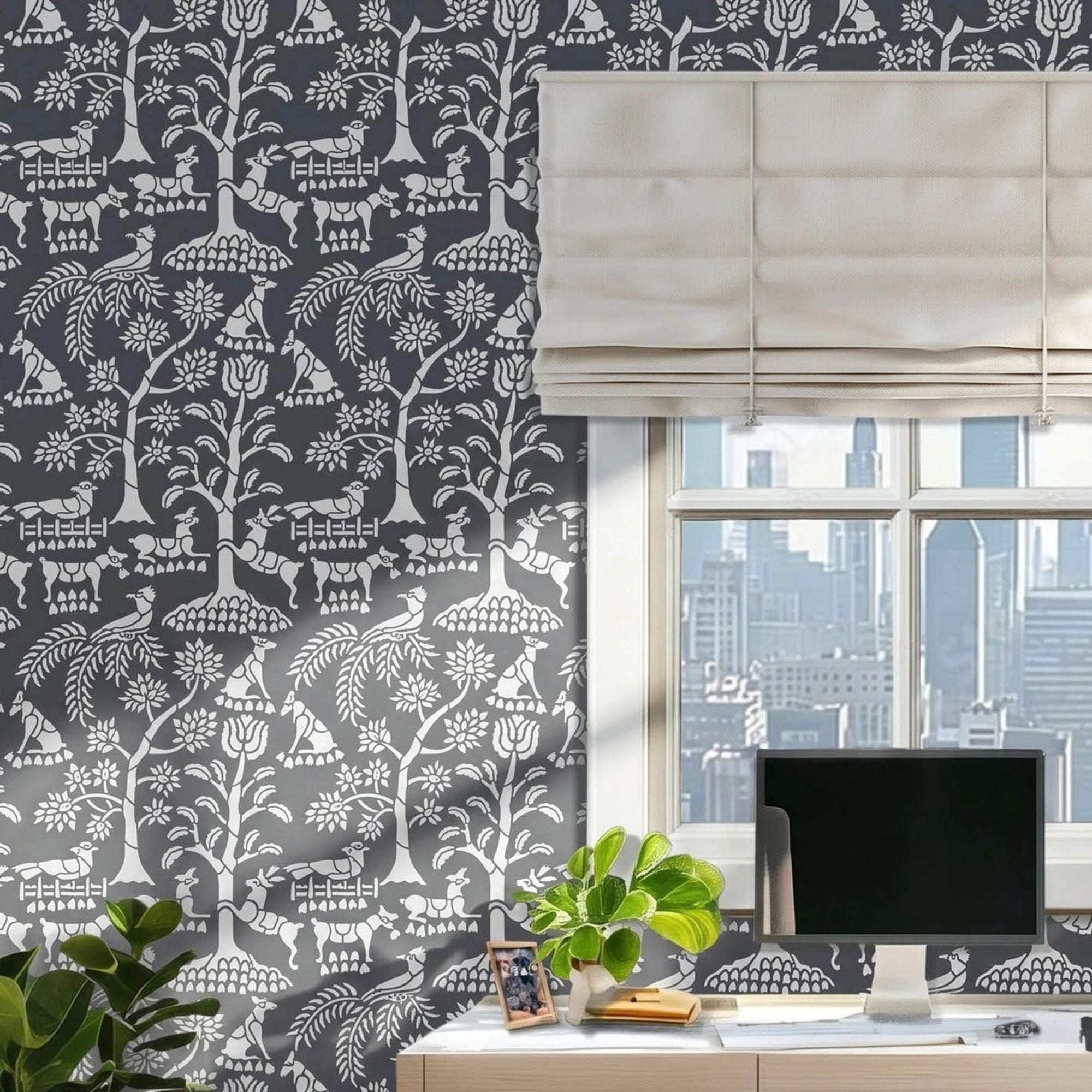 Enchanted forest wall stencil  featured in an office with a window and a beige roman shade, a desk with a computer monitor, small plants, and natural light highlighting the charcoal and light grey painted stencil on the wall.