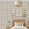 Enchanted forest wall stencil in a bedroom with a bed with a headboard , framed  prints hang on the wall, with a hanging drum lamp and bedside tables with lamps, and natural light highlighting the olive green and peach painted stencil on the wall.