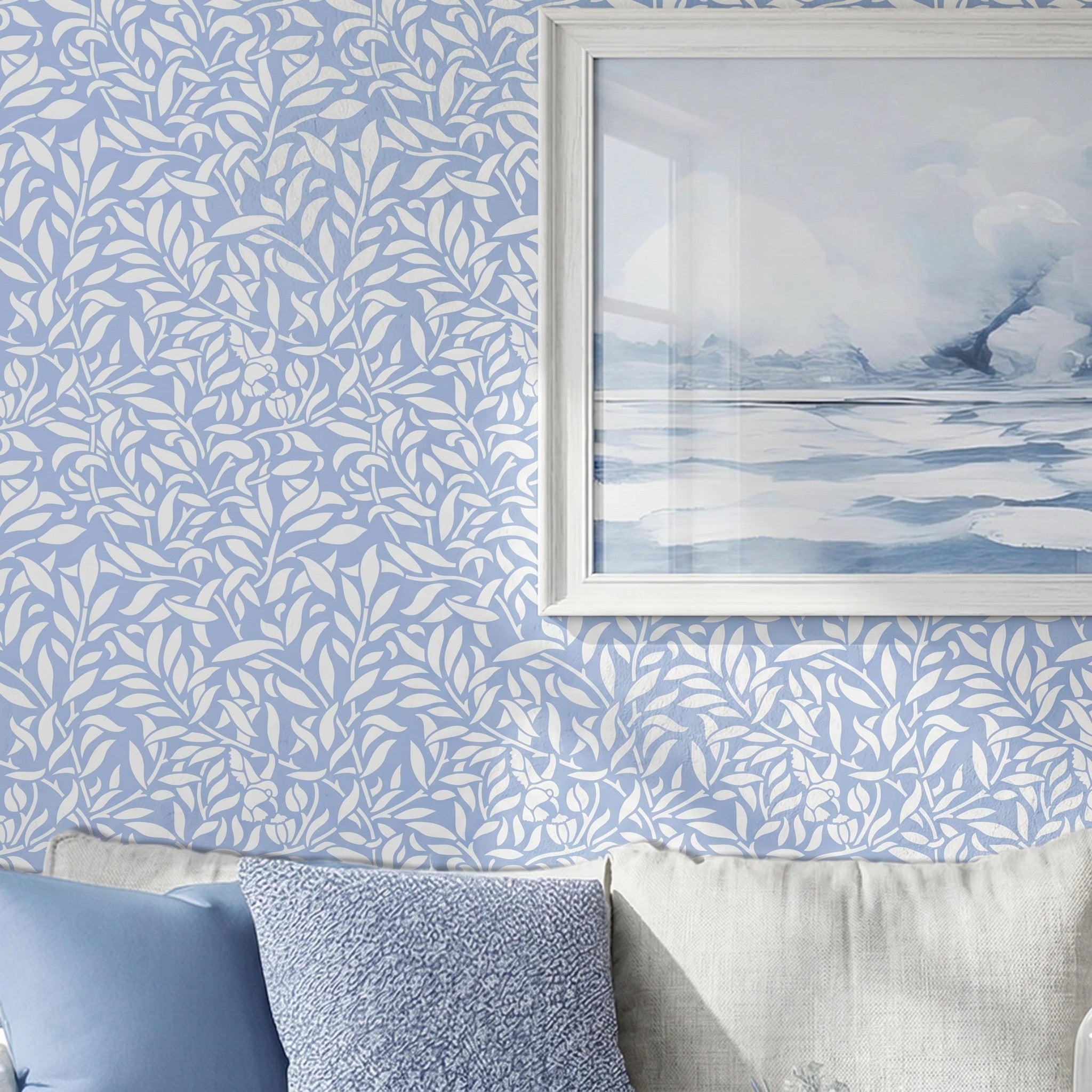 Hummingbird stencil on a wall above a sofa with blue and textured pillows, with a framed landscape print hanging on the wall, natural soft light highlighting the blue and white painted stencil on the wall.