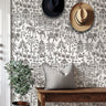 Indian village wall stencil applied in a entryway featuring a wooden bench, two hats hanging on the wall, a plant, a front door, and natural light highlighting the gray and white wall stencil painted on the wall.