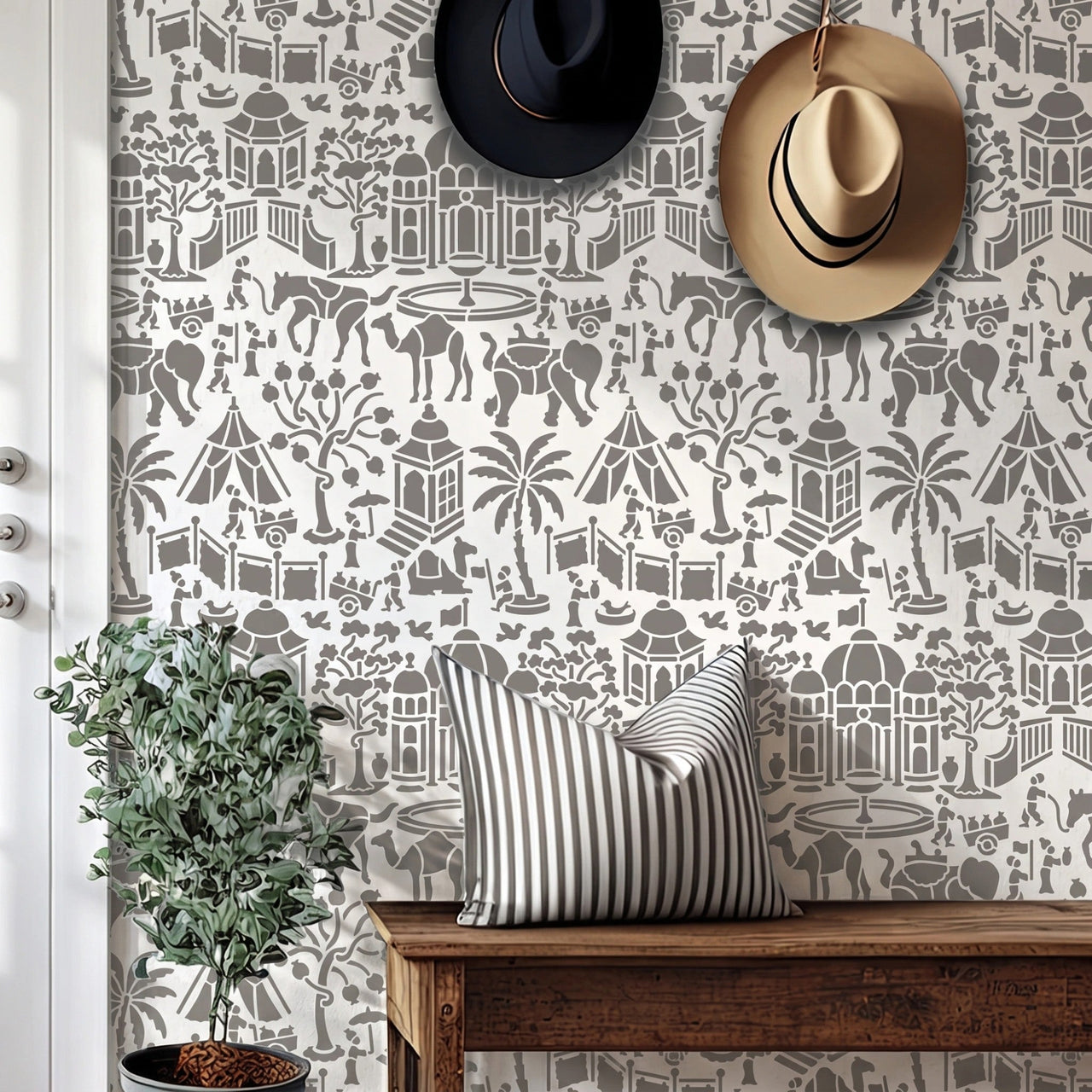 Indian village wall stencil applied in a entryway featuring a wooden bench, two hats hanging on the wall, a plant, a front door, and natural light highlighting the gray and white wall stencil painted on the wall.
