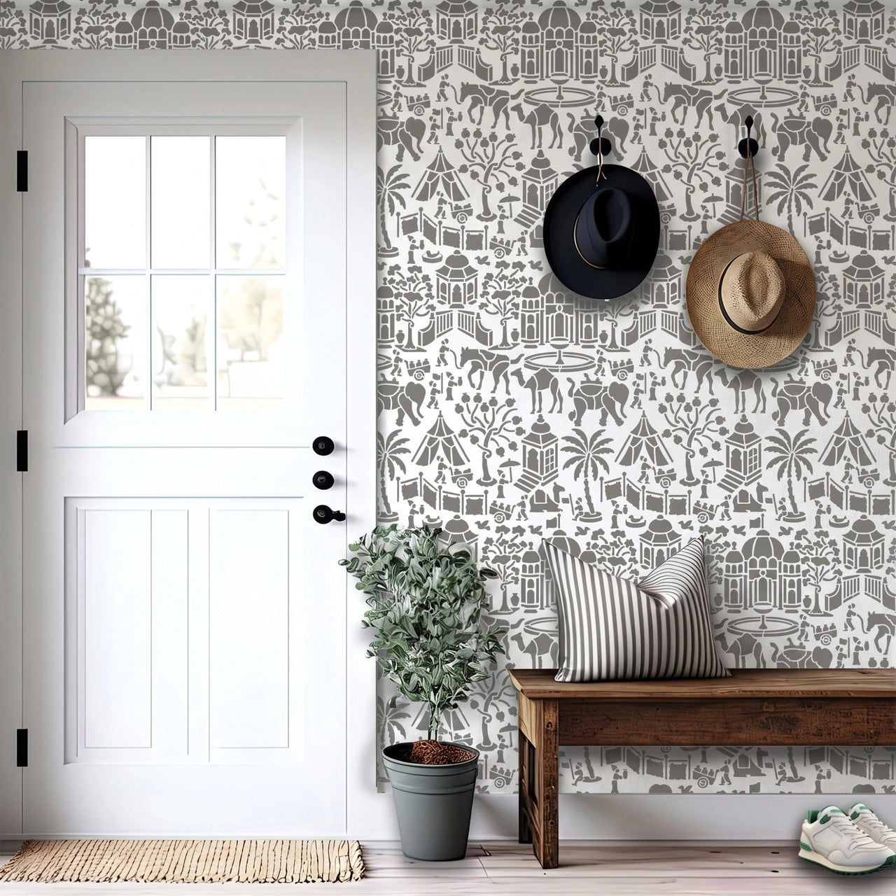 Indian village wall stencil applied in a entryway featuring a wooden bench, two hats hanging on the wall, a plant, a front door, and natural light highlighting the gray and white wall stencil painted on the wall.