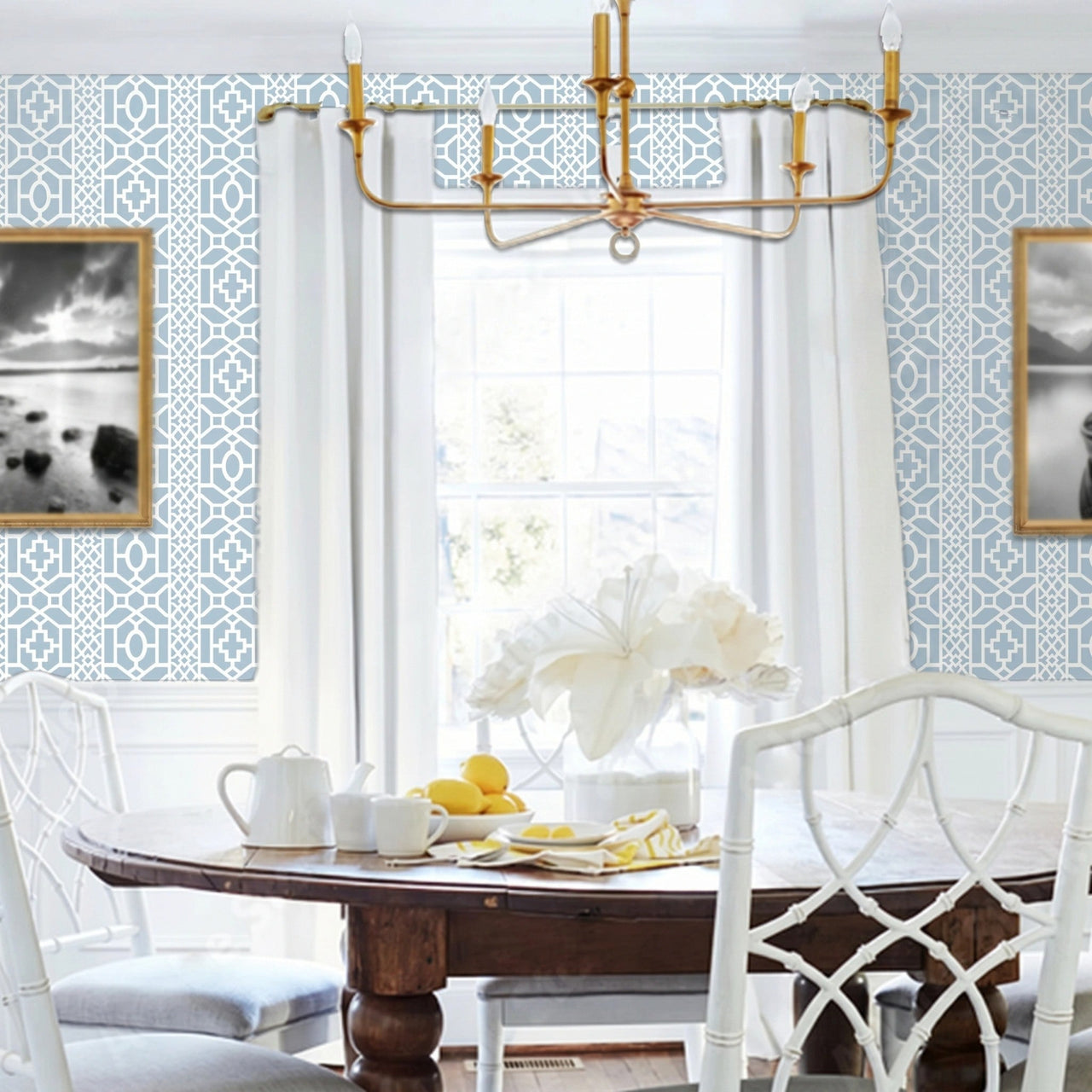 Moroccan Lattice wall stencil applied in a dining room featuring a round wooden table with white chairs, a gold chandelier, a window with curtains, and natural light highlighting the light blue and white geometric stencil on the wall.