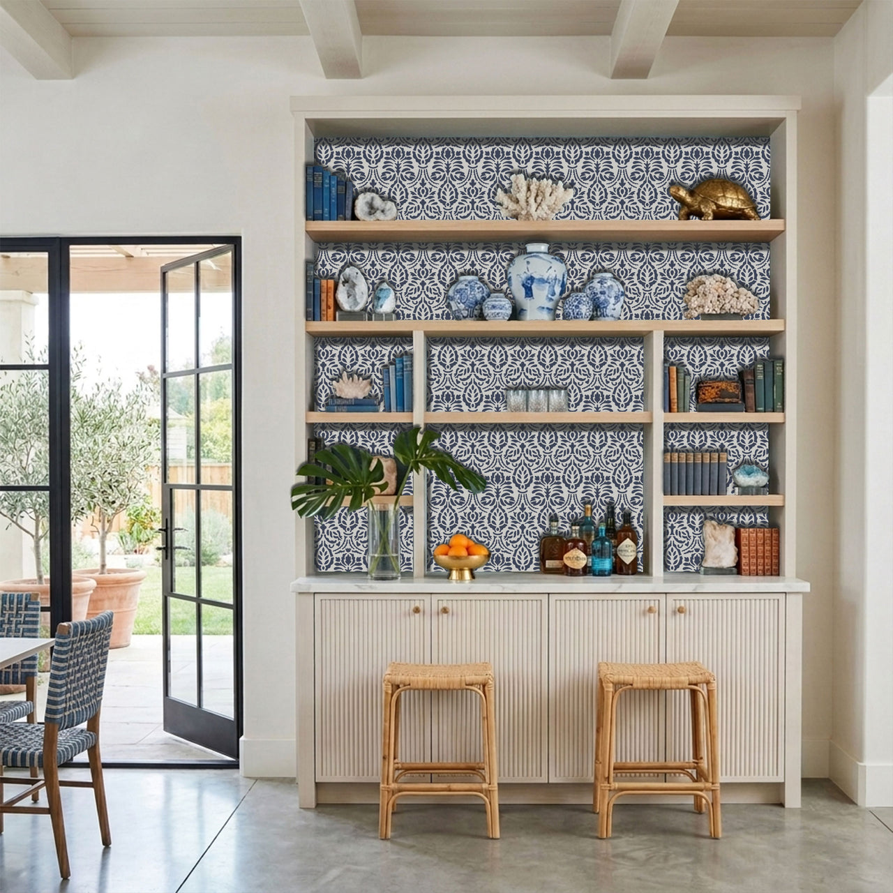 Spear thistle wall stencil applied in a built-in shelving unit with, wood shelves, decorative vases, books, bottles, and natural light highlighting the dark blue and light blue painted stencil in the built-in shelving unit.