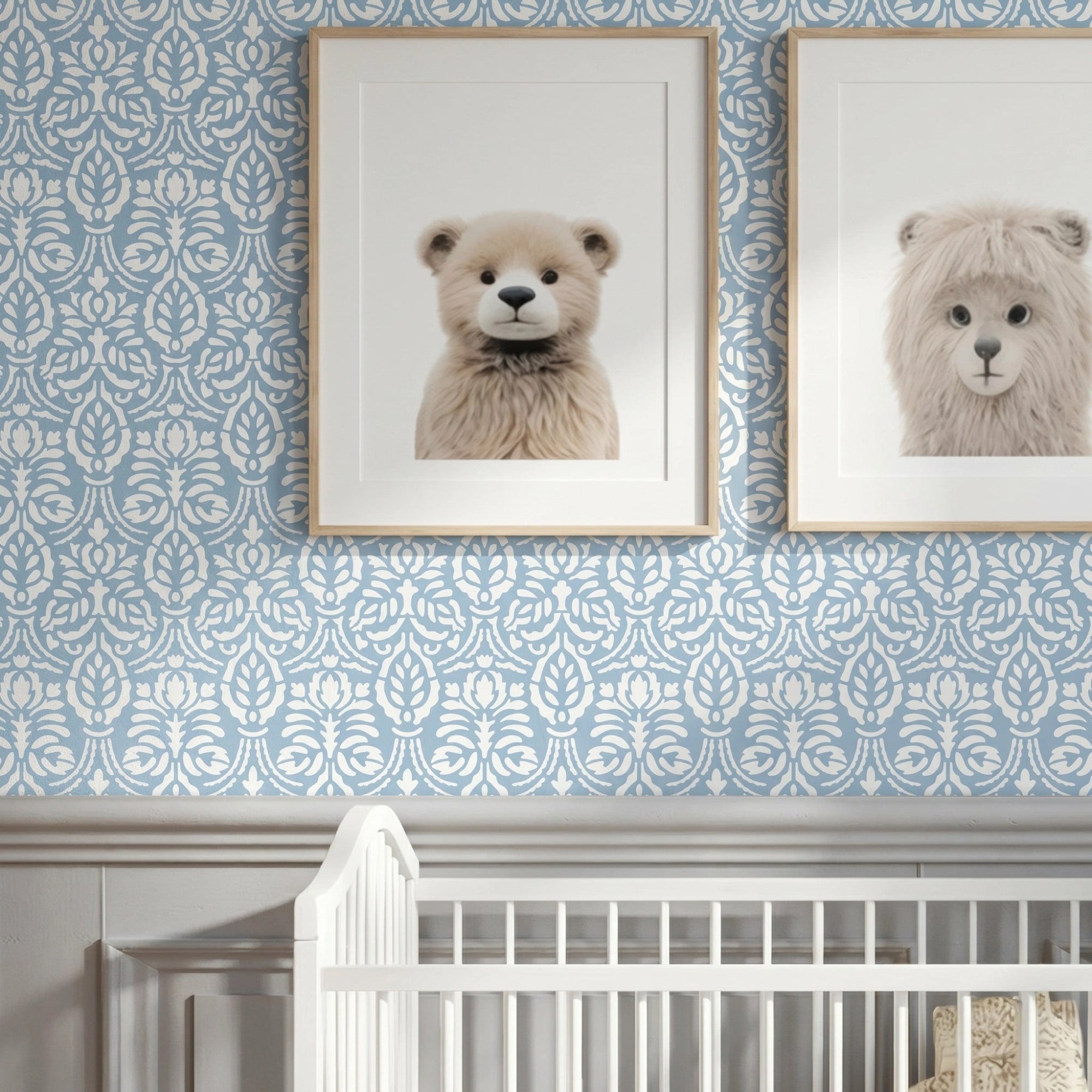 Spear thistle wall stencil in a styled nursery wall featuring, two framed art prints of teddy bears, and a white wooden crib at the bottom, and natural light highlighting the blue and white floral painted stencil on the wall.