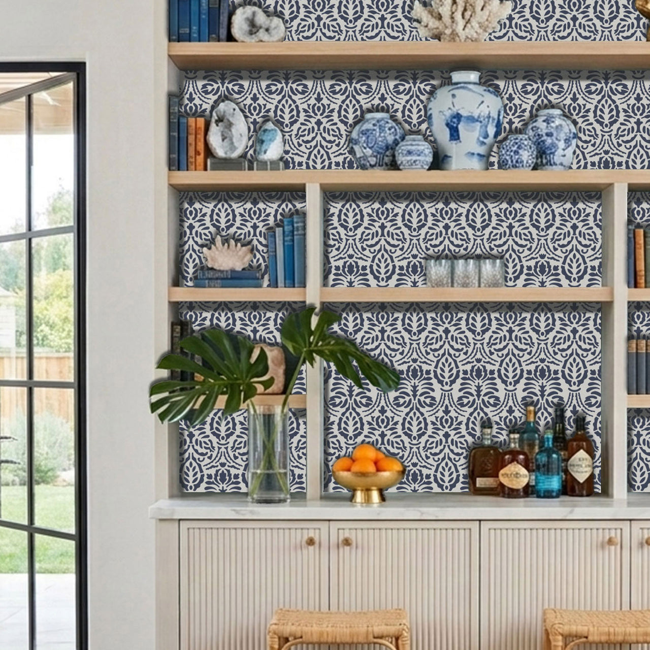 Spear thistle wall stencil applied in a built-in shelving unit with, wood shelves, decorative vases, books, bottles, and natural light highlighting the dark blue and light blue painted stencil in the built-in shelving unit.