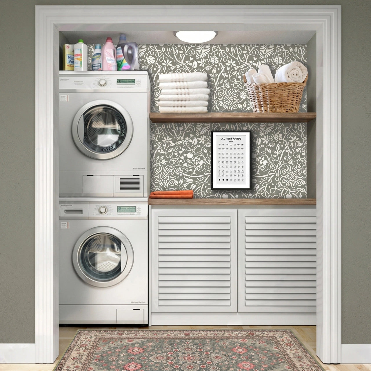 Swedish botanical wall stencil in a laundry machine in a entryway, wooden shelves, folded towels, a basket, and a framed image of laundry instruction symbols, with natural light highlighting the olive green and white painted stencil on the wall.
