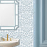 Thistle and Vine wall stencil pattern applied in a powder room setting with a white sink, gold faucet, and a light blue-framed mirror, and natural light highlighting the blue and white painted stencil on the wall.