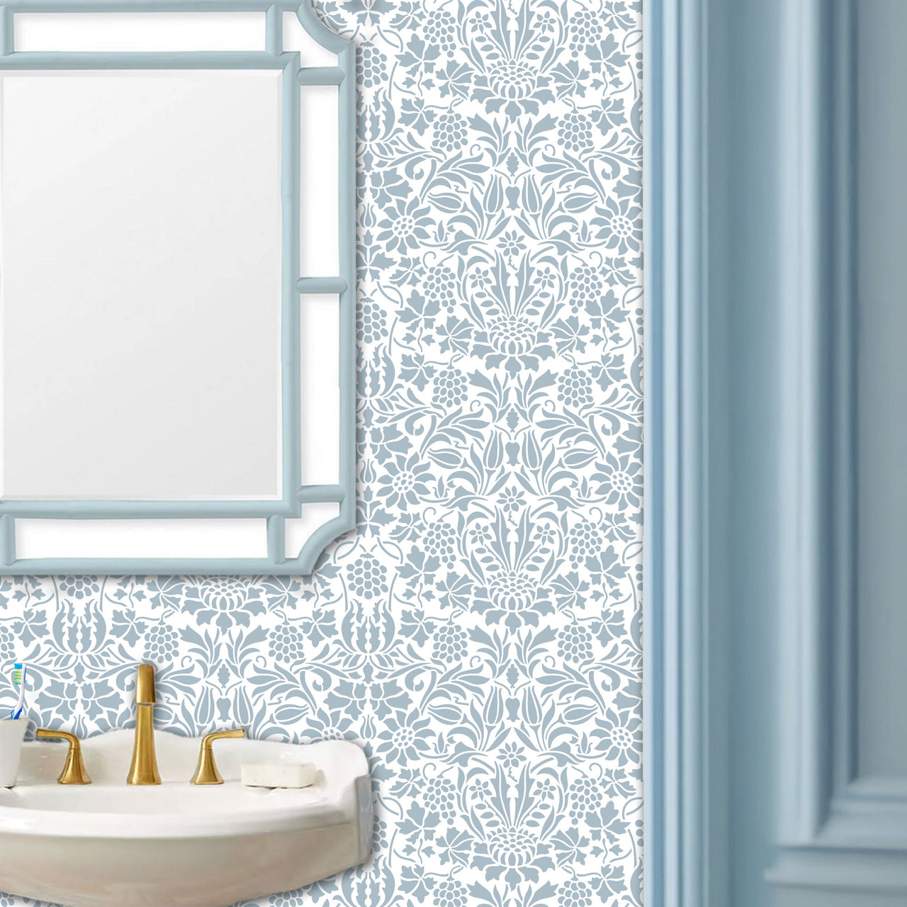 Thistle and Vine wall stencil pattern applied in a powder room setting with a white sink, gold faucet, and a light blue-framed mirror, and natural light highlighting the blue and white painted stencil on the wall.