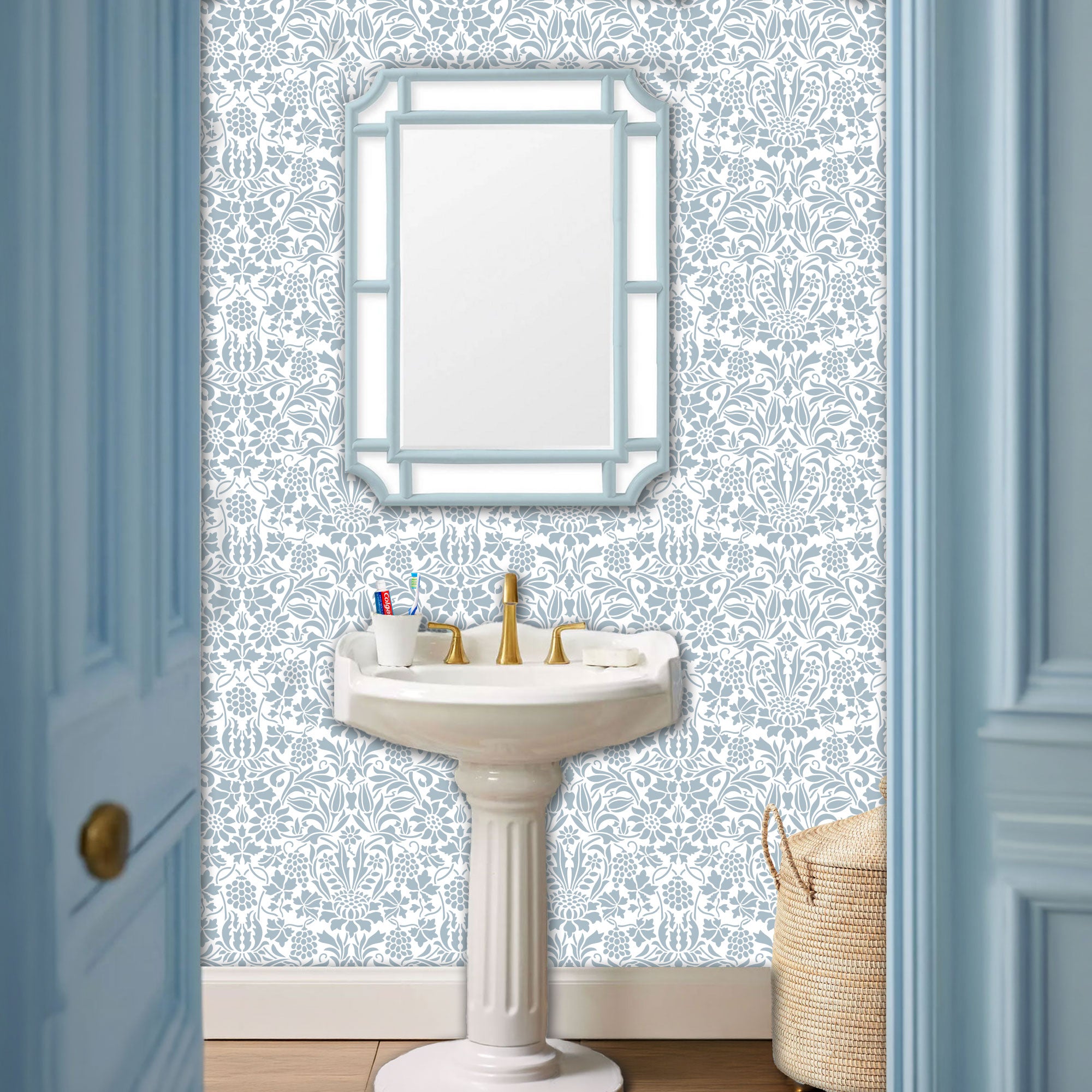 Thistle and Vine wall stencil pattern applied in a powder room setting with a white sink, gold faucet, and a light blue-framed mirror, and natural light highlighting the blue and white painted stencil on the wall.