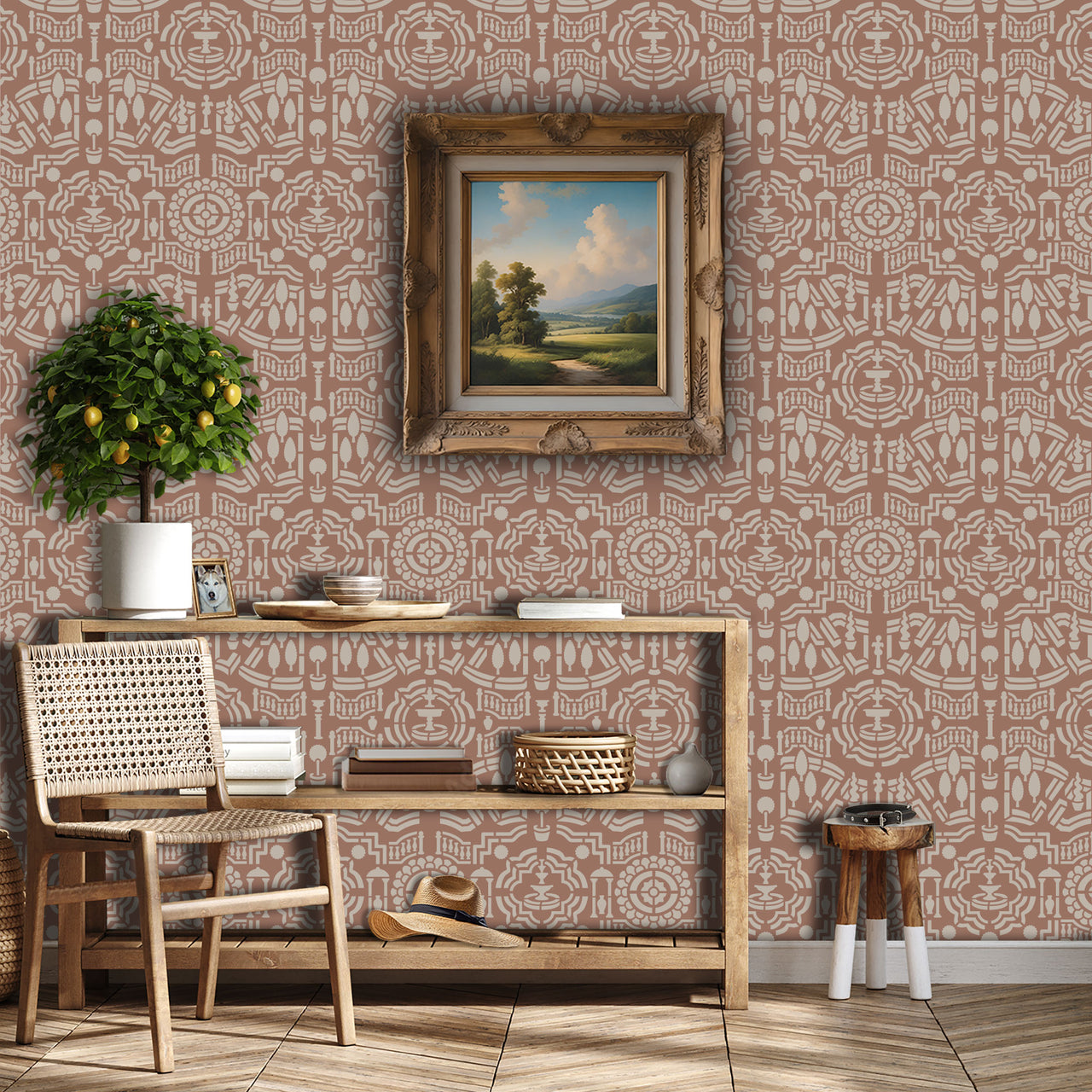 Topiary garden wall stencil applied in a hallway with a framed landscape painting hanging above a wooden table holding books and decorative objects, a chair, a plant and soft light highlighting the dusty rose and beige painted stencil on the wall.