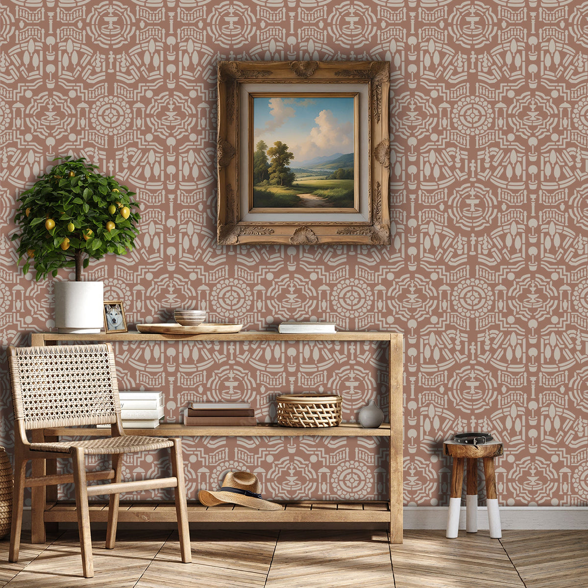 Topiary garden wall stencil applied in a hallway with a framed landscape painting hanging above a wooden table holding books and decorative objects, a chair, a plant and soft light highlighting the dusty rose and beige painted stencil on the wall.