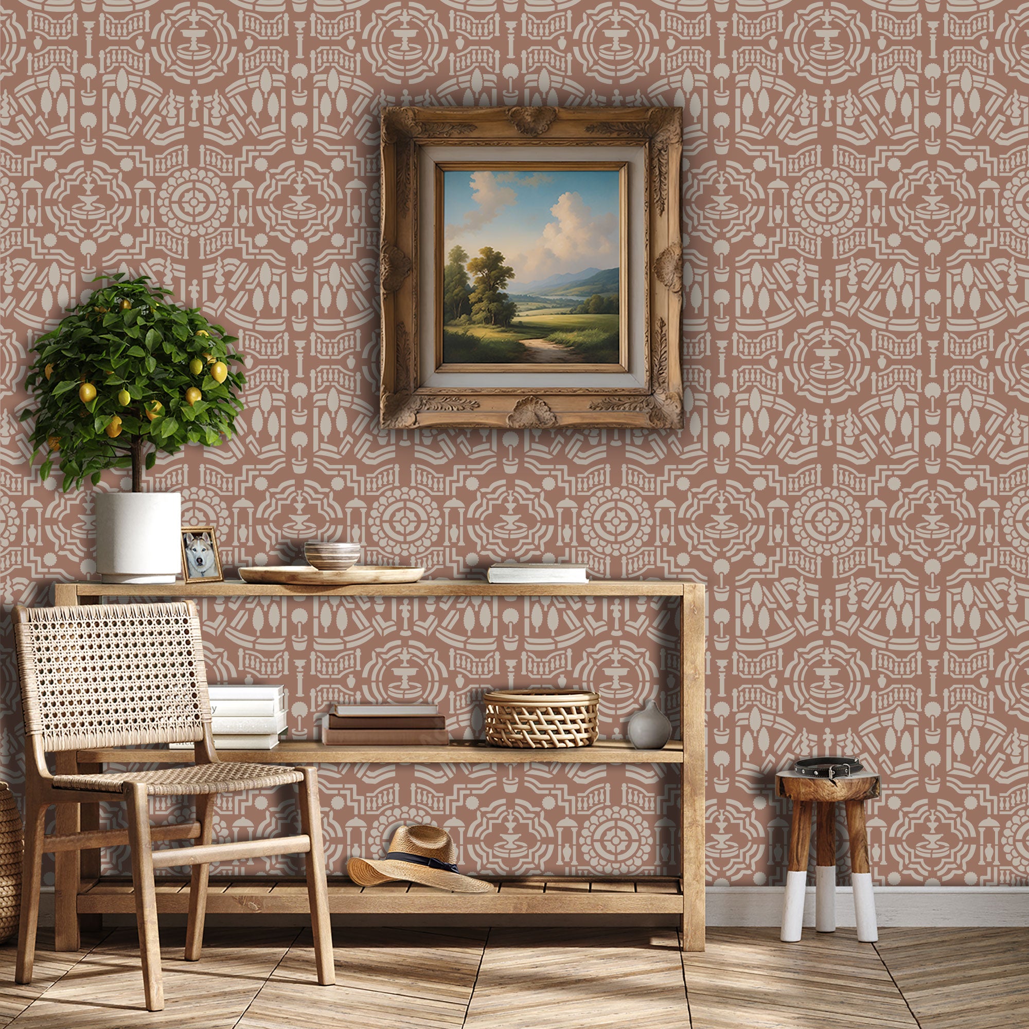 Topiary garden wall stencil applied in a hallway with a framed landscape painting hanging above a wooden table holding books and decorative objects, a chair, a plant and soft light highlighting the dusty rose and beige painted stencil on the wall.