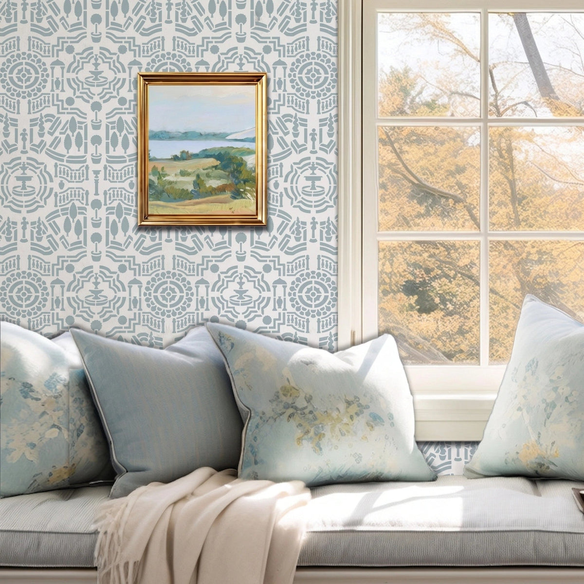 Topiary Garden wall stencil featuring a window seat cushion, a landscape paintings on the wall, and a window with natural light highlighting the light blue and dark blue painted stencil on the wall.
