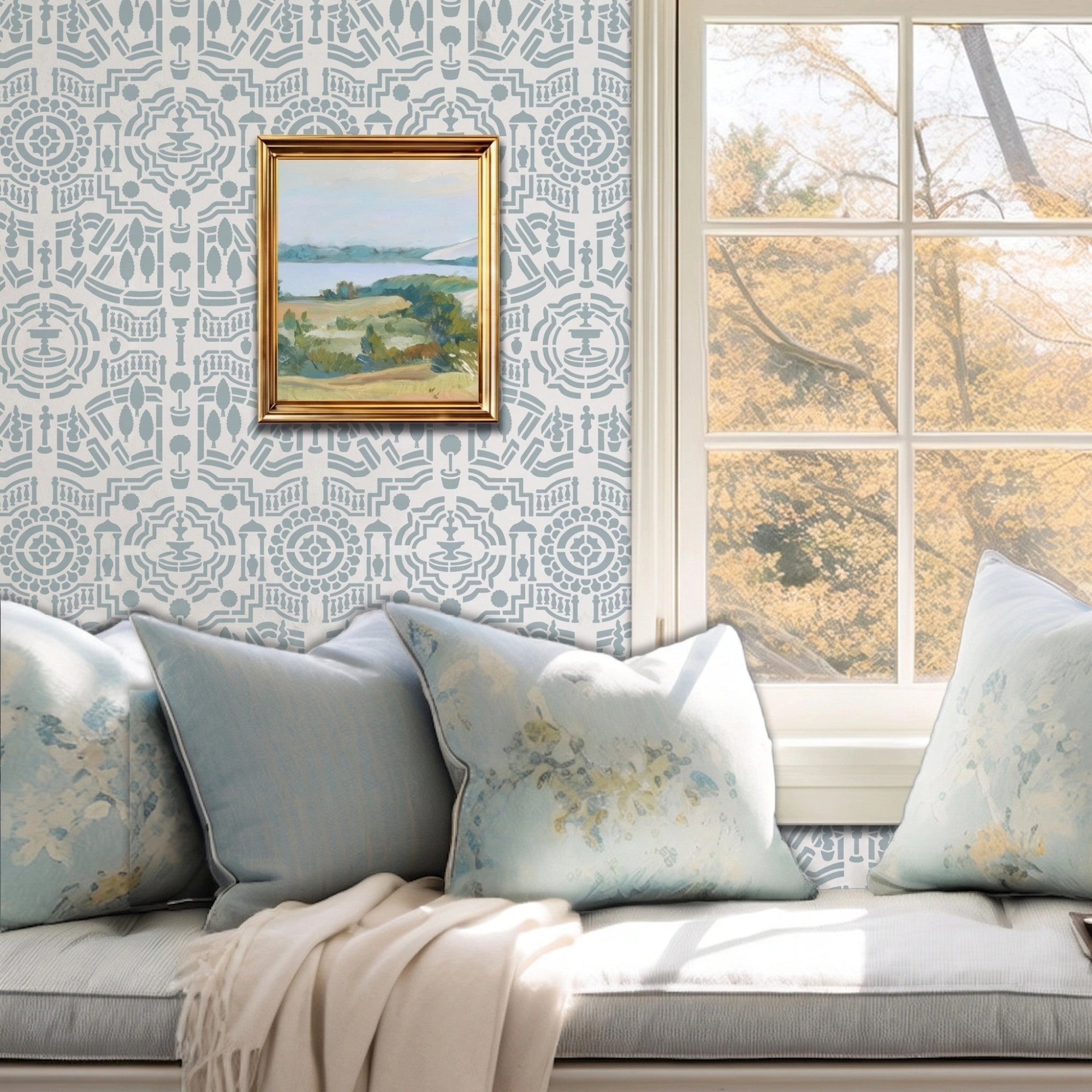 Topiary Garden wall stencil featuring a window seat cushion, a landscape paintings on the wall, and a window with natural light highlighting the light blue and dark blue painted stencil on the wall.