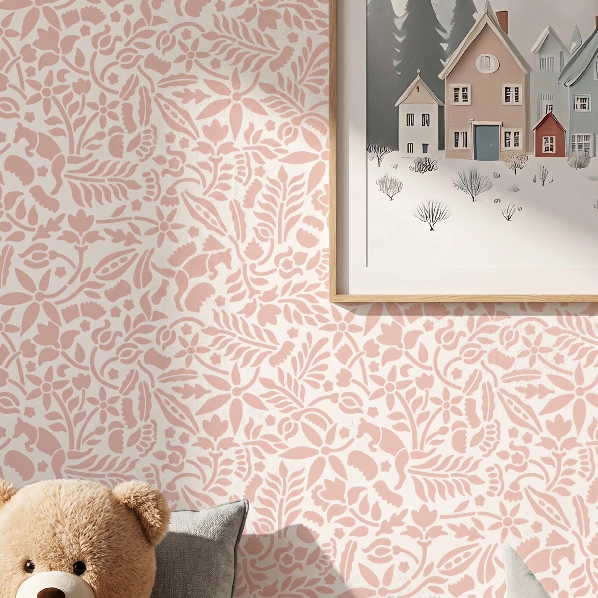 Woodland Foxes wall stencil applied in a soft pink and white nursery, shown behind a framed woodland village print with a teddy bear and pillows below, and the soft pink and white painted stencil on the wall.