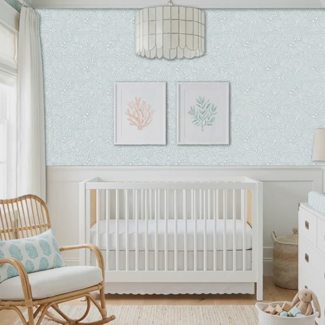 Video of abstract seashells wall stencil applied behind a white crib and natural light highlighting the bluish green and white painted stencil on the wall. Pregnant woman walks into nursery followed by a dog, touches the wall stencil in admiration, pets the dog and they leave the room.