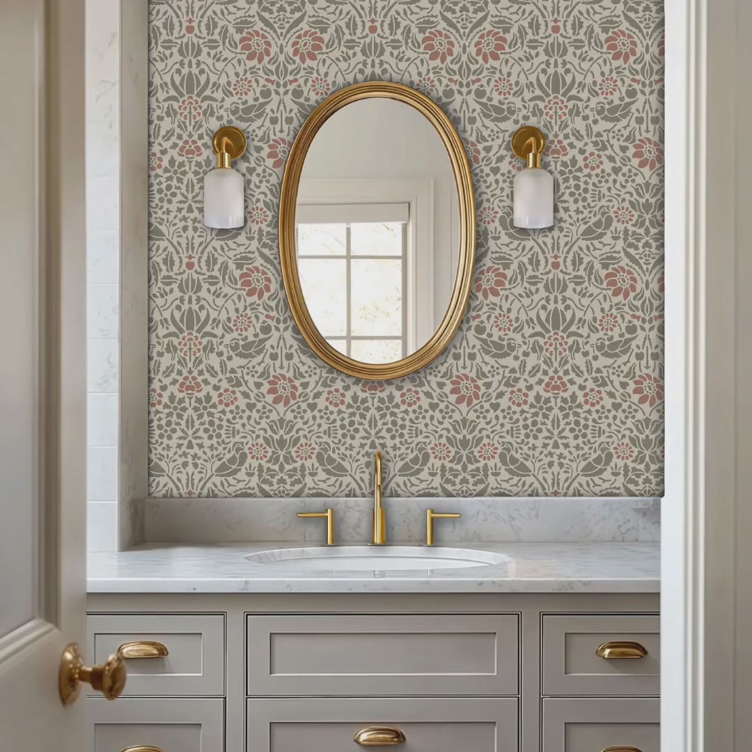 Video of birds and berries wall stencil applied in a powder room with an oval mirror with a gold frame featuring a repeating pattern of birds, flowers, and leaves in muted green and pink tones painted stencil on the wall. Woman enters, places towels on the countertop and exits.