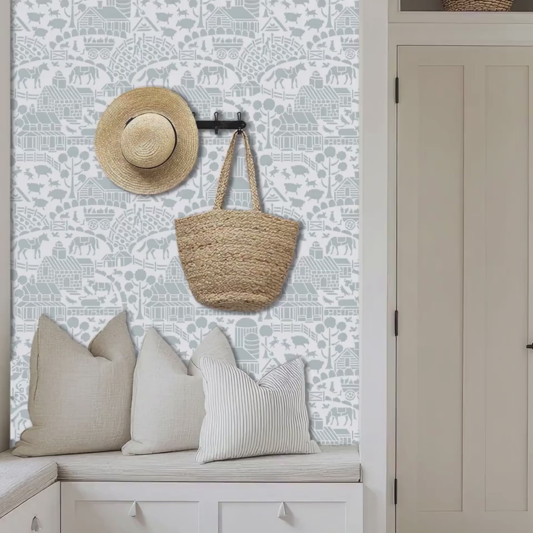 Video of day at the farm farmhouse wall stencil applied in a mudroom with pillows, a hat and basket hanging on the wall, and natural light highlighting the light blue and white painted stencil on the wall. Woman opens the door and enters the room.