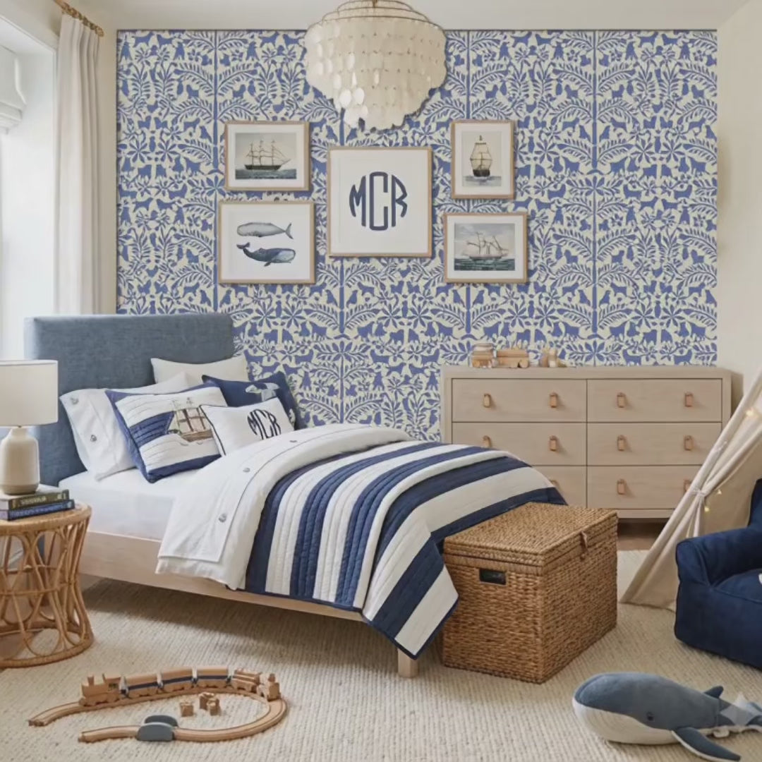 Video of dogs in the garden wall stencil applied in a children's bedroom featuring a bed with navy and white striped bedding, framed prints, a wood dresser, and a chandelier, and natural light highlighting the dark blue and beige painted stencil on the wall. Boy walks into the bedroom, followed by a beagle. He sits on the floor and plays with his dog.