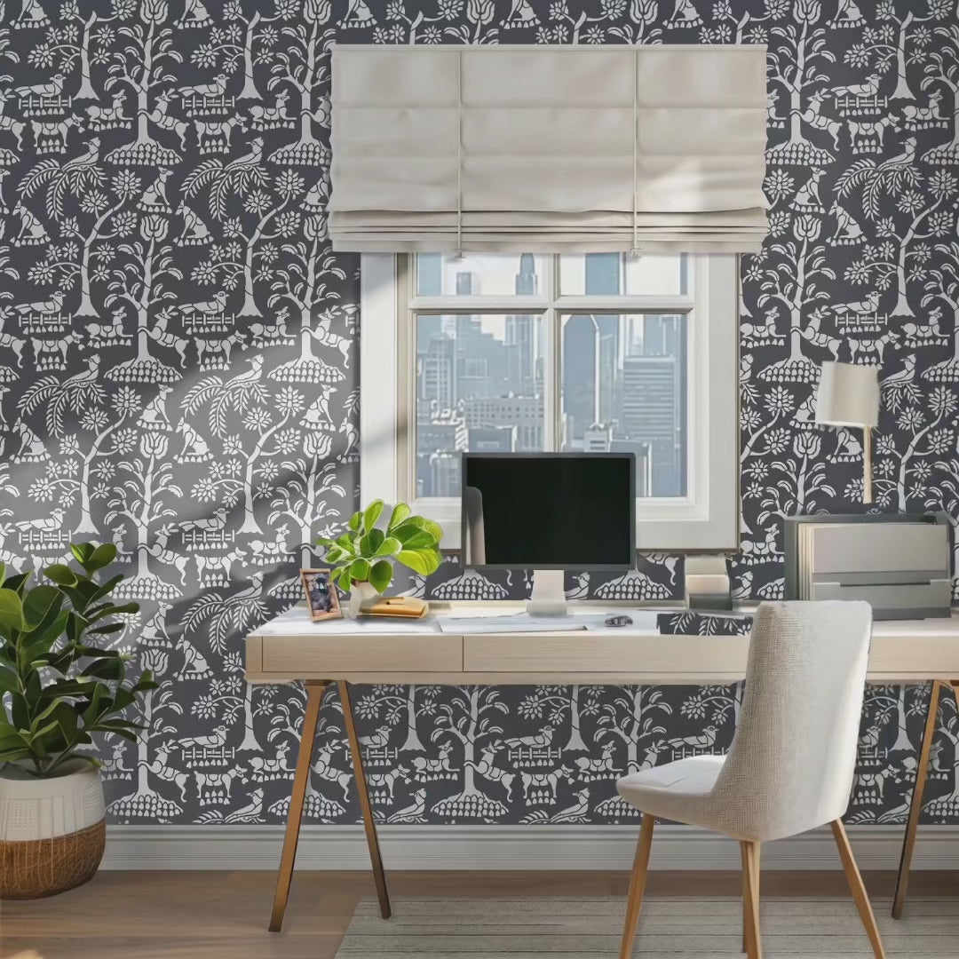 Video of Enchanted forest wall stencil  featured in an office with a window and a beige roman shade, a desk with a computer monitor, plants, a chair, and natural light highlighting the charcoal and light grey painted stencil on the wall. Woman walks in and sits in chair and picks up her cell phone.